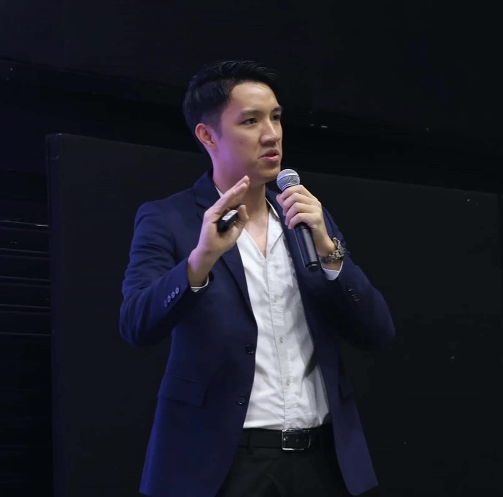 Daren Tan speaking on stage, microphone in hand, in a navy blazer